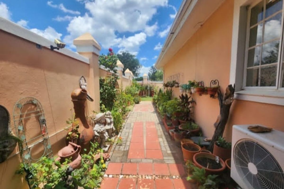 A side garden pathway featuring terracotta paving, perimeter walling, and an external air conditioning unit.