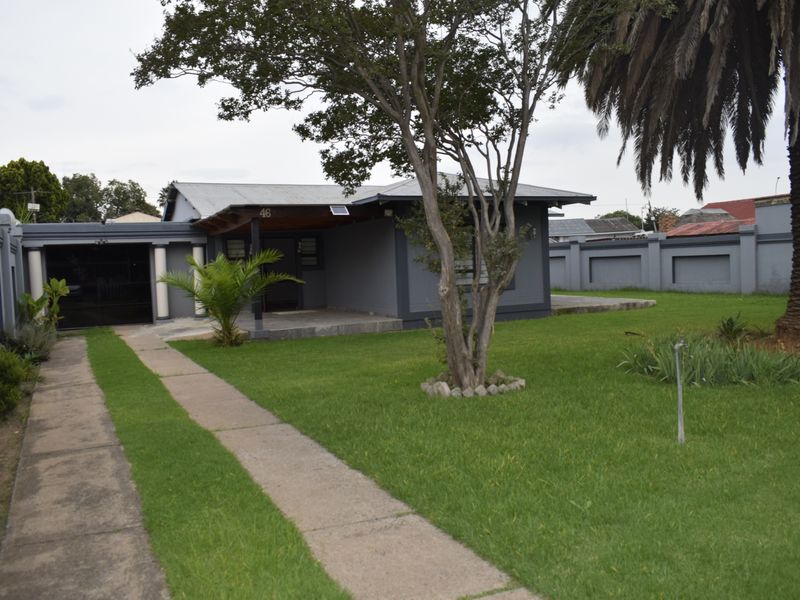 Front view of a single-story house featuring a paved driveway, covered entrance porch, and a well-maintained garden with perimeter boundary walls.