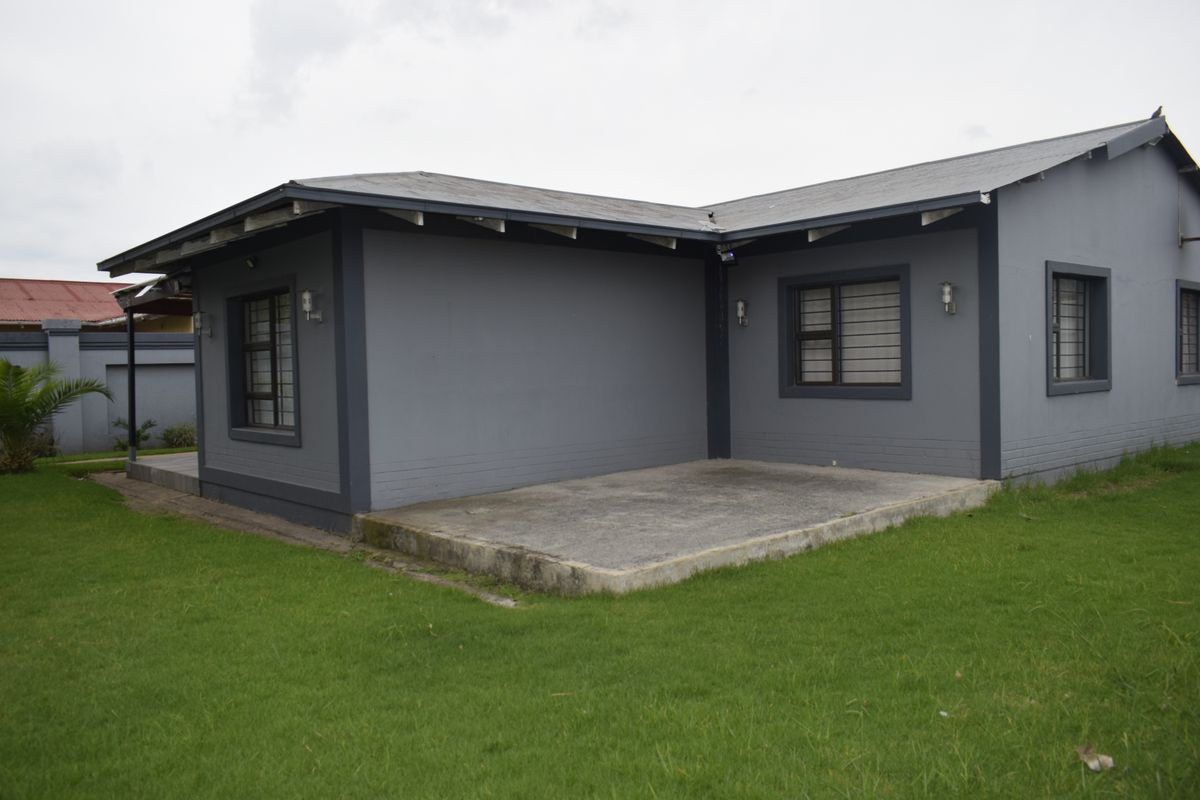 Rear view of the house featuring a concrete patio area, security bars on windows, and a well-maintained lawn.