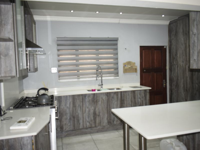 Modern kitchen featuring dark wood-grain cabinetry, stone countertops, a gas hob with extractor, and recessed lighting.