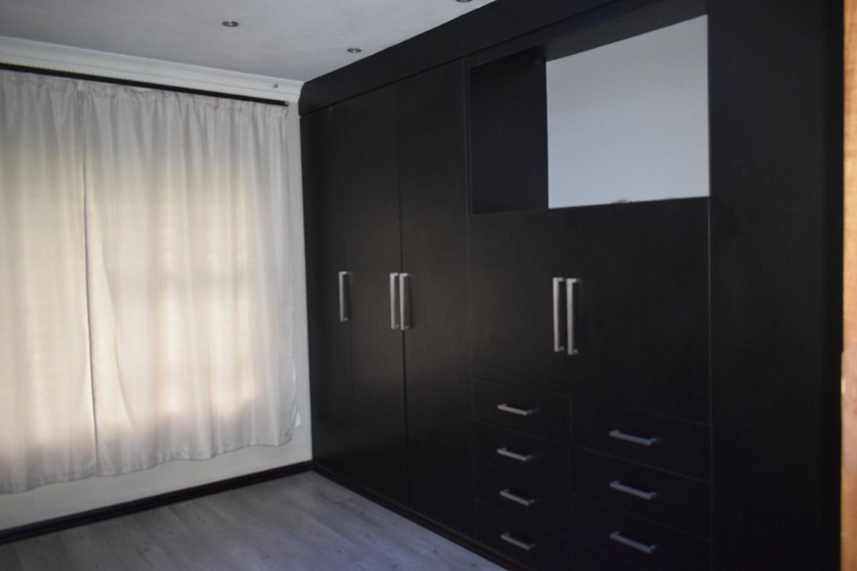 A bedroom featuring dark built-in cupboards with integrated drawers and shelving, complemented by light-toned laminate flooring and recessed ceiling lighting.
