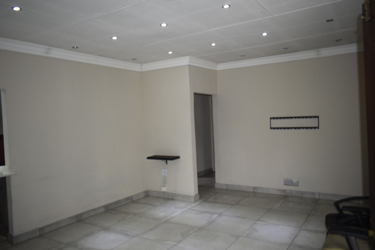 An empty living room featuring tiled flooring, recessed ceiling downlights, and neutral wall finishes, providing a blank canvas for interior design.