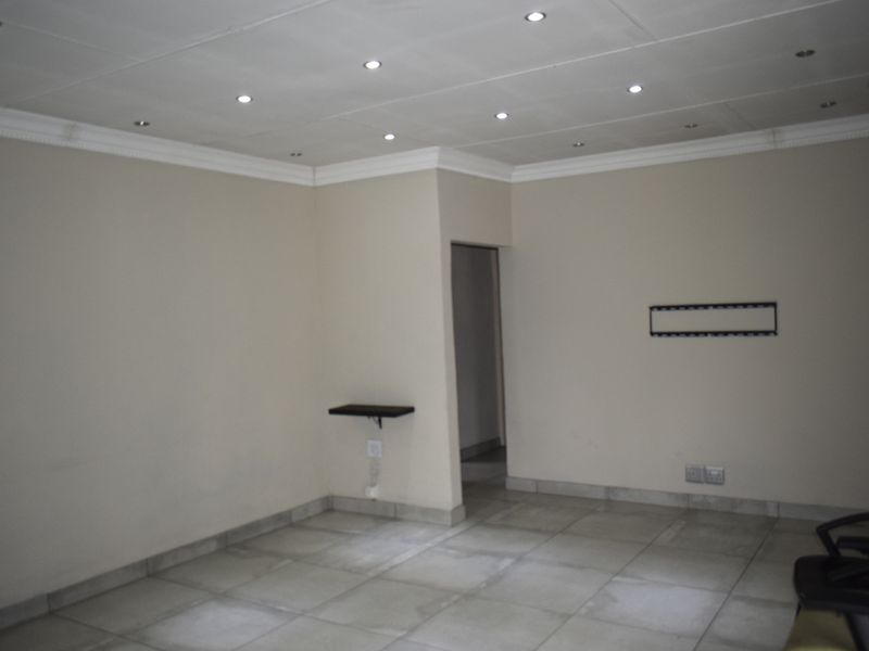An empty living room featuring tiled flooring, recessed ceiling downlights, and neutral wall finishes, providing a blank canvas for interior design.