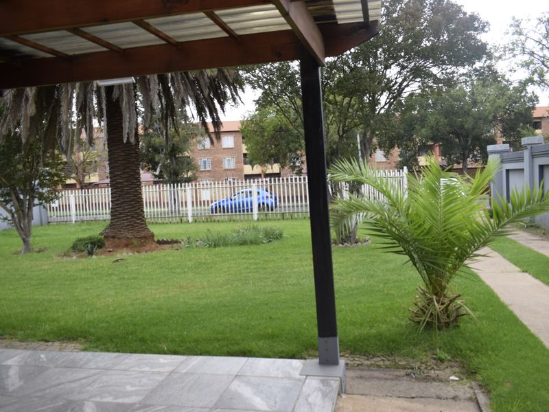 A covered patio area featuring tiled flooring and a timber pergola, overlooking a private garden with established trees and perimeter fencing.