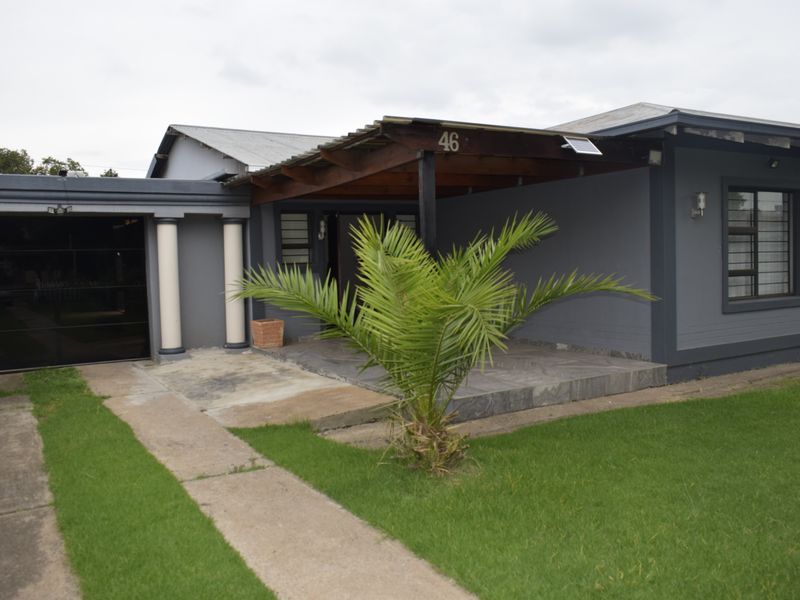 Front elevation of a house featuring a covered patio, attached garage, and a paved driveway set within a lawned garden.