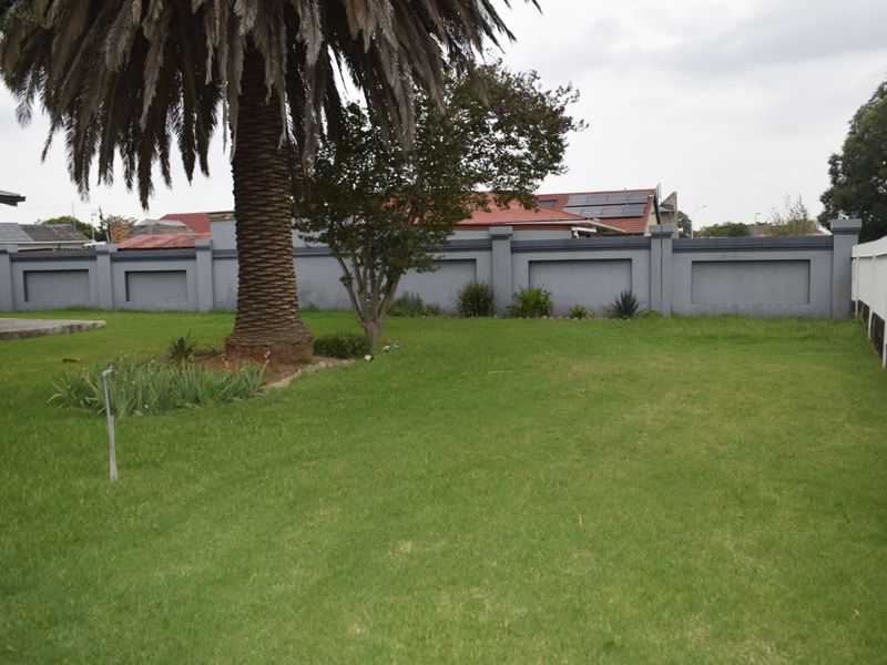 A well-maintained private garden featuring a large lawn, mature palm tree, and secure perimeter walling.