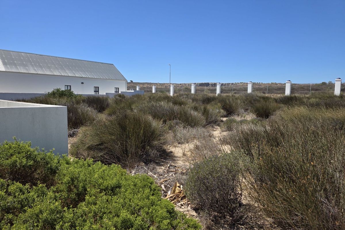 A view of the vacant residential land featuring native shrubbery, a perimeter fence with pillars, and an adjacent building structure.