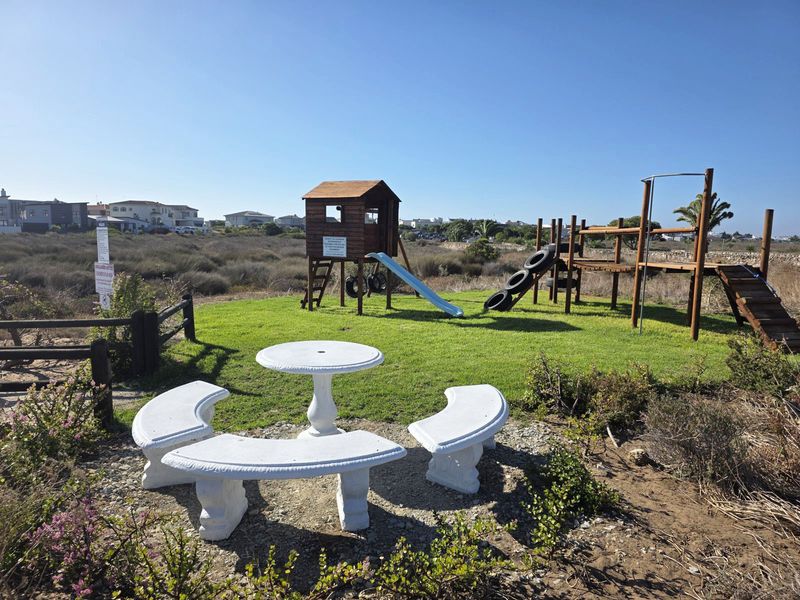 A communal outdoor recreational area featuring a children's wooden play structure, slide, and fixed concrete bench seating set within a landscaped garden space.