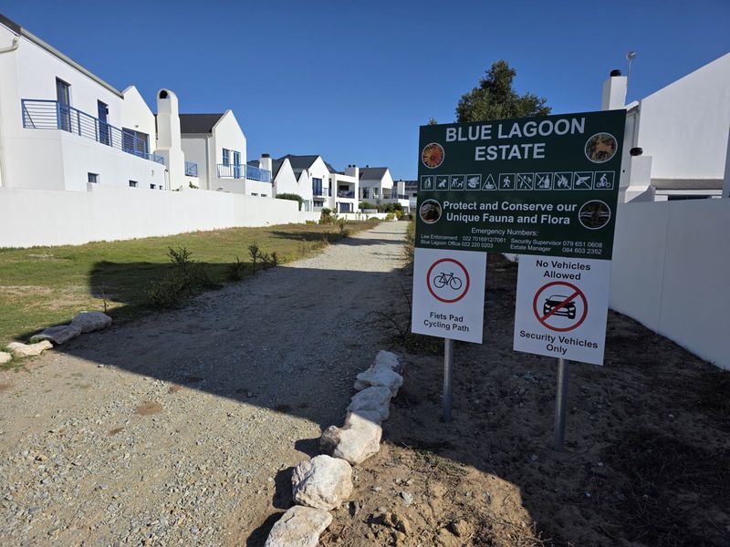 A view of a gravel access path within the Blue Lagoon Estate, featuring residential buildings and estate signage.