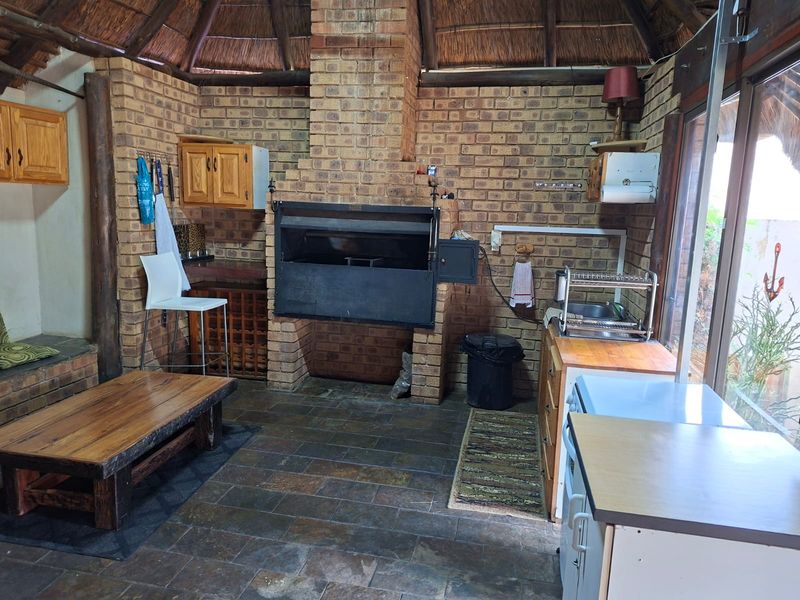 Covered outdoor entertainment area featuring a built-in braai, rustic exposed brick walls, and a traditional thatch roof with slate flooring.