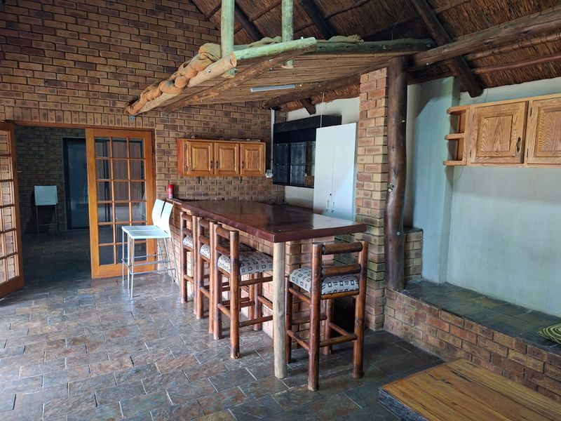 Rustic covered patio area featuring a thatched roof, exposed brickwork, slate flooring, and a built-in wooden bar with overhead storage cabinetry.