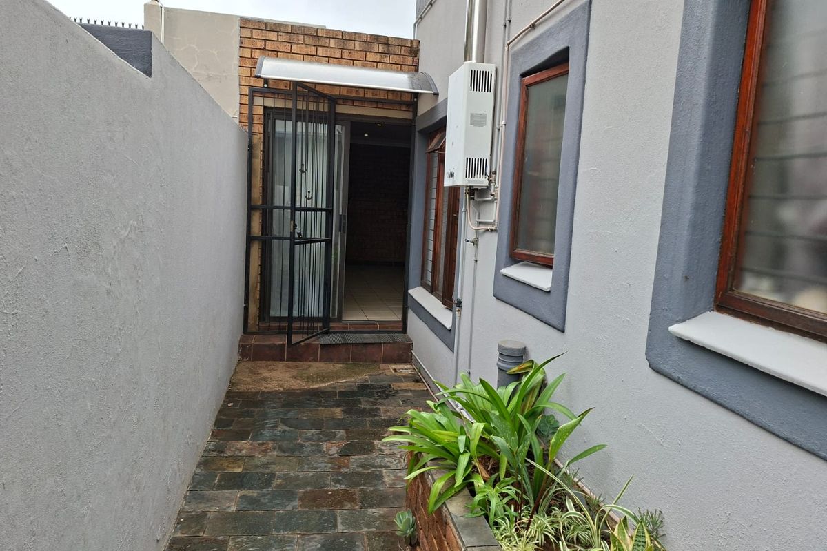 Rear exterior walkway featuring slate paving, a brick planter, and a wall-mounted gas geyser leading to a secure entrance.