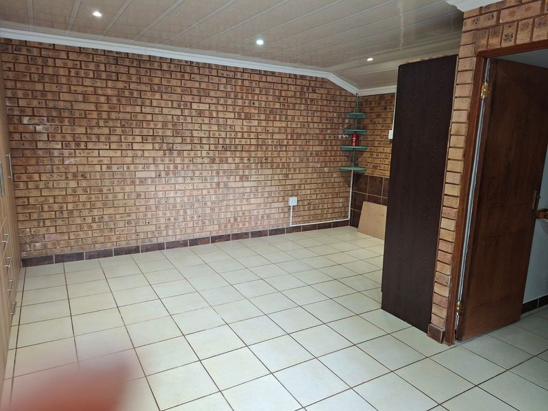 An empty bedroom featuring exposed brick walls, tiled flooring, recessed ceiling lights, and a built-in cupboard.