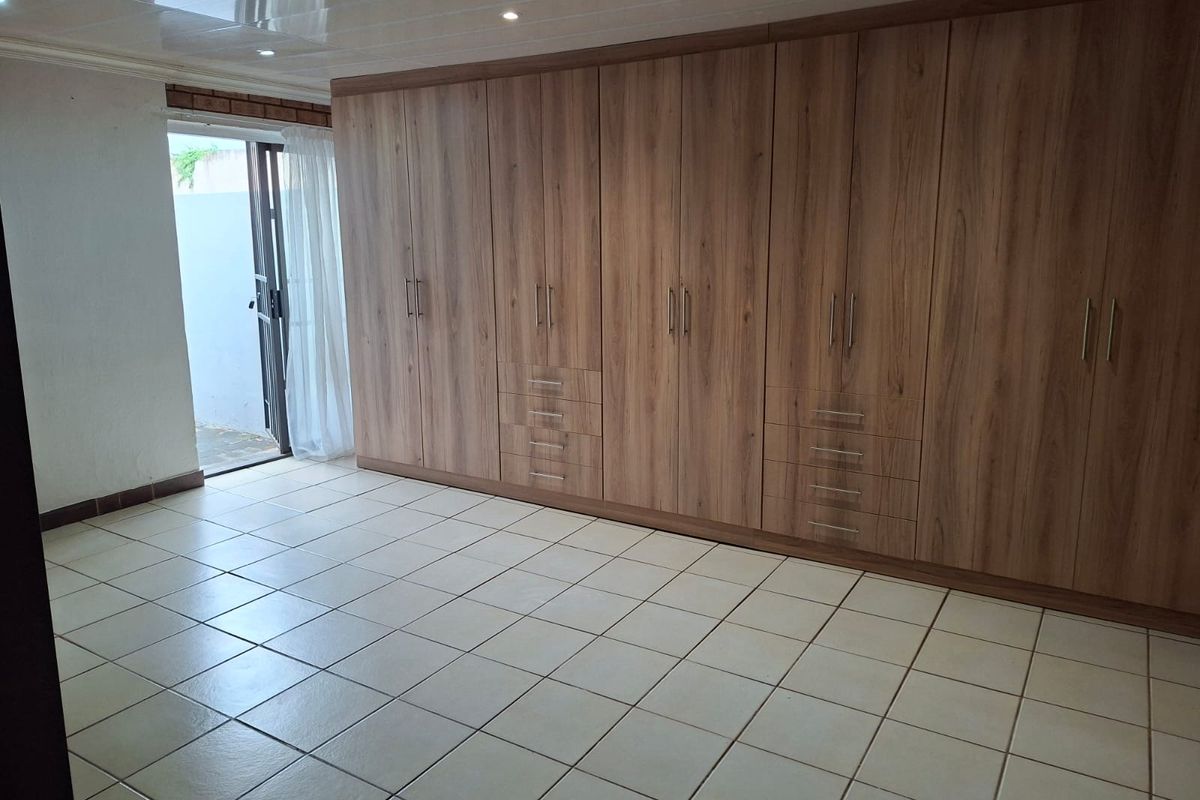 Spacious bedroom featuring extensive built-in wooden cabinetry, neutral tiled flooring, and direct access to an outdoor area through a sliding door.