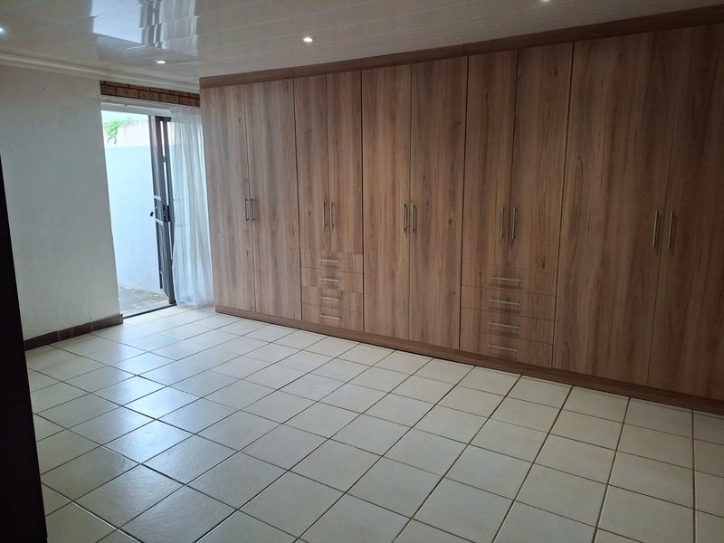 Spacious bedroom featuring extensive built-in wooden cabinetry, neutral tiled flooring, and direct access to an outdoor area through a sliding door.