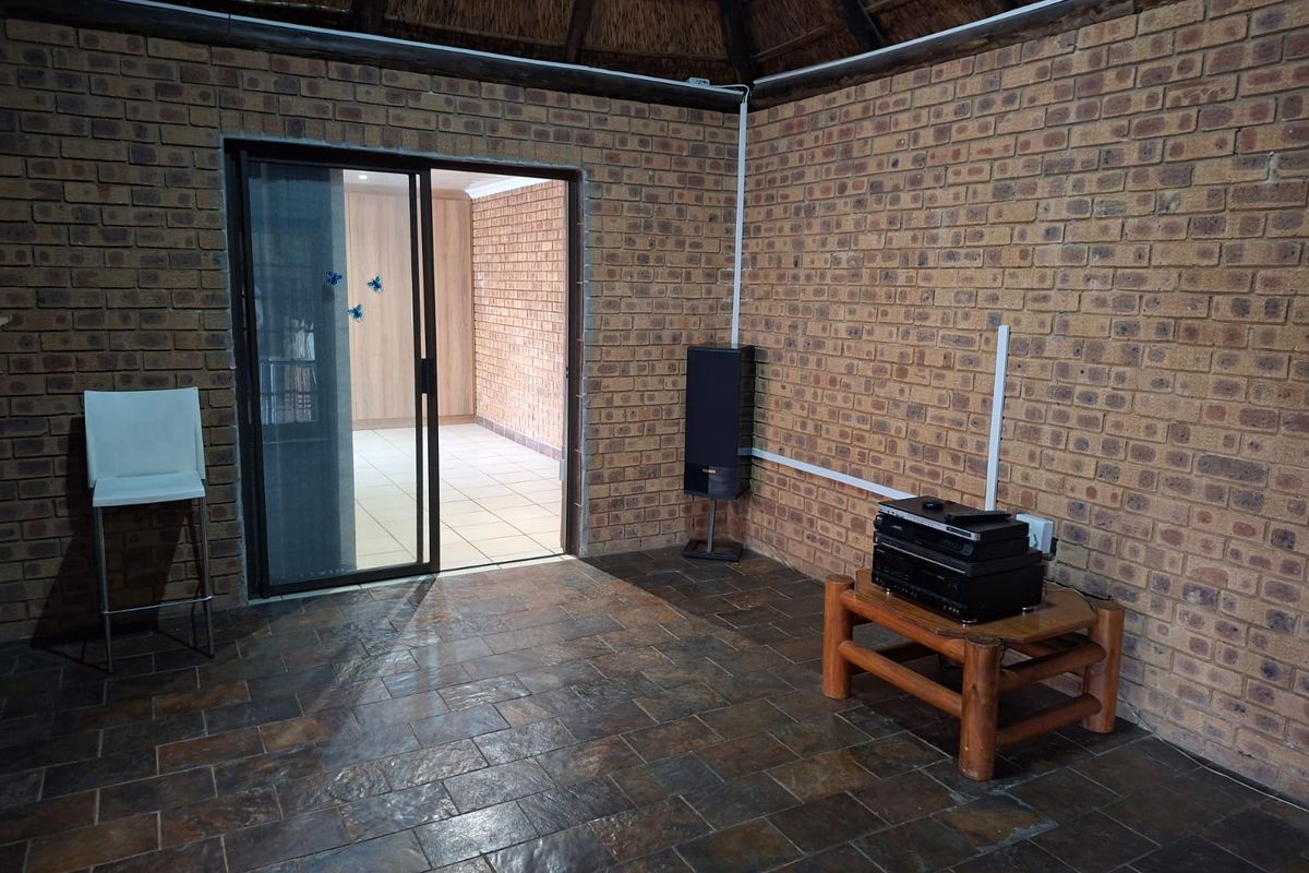Living area featuring rustic exposed brick walls, slate tile flooring, and a traditional thatched roof ceiling with access to an adjoining room.