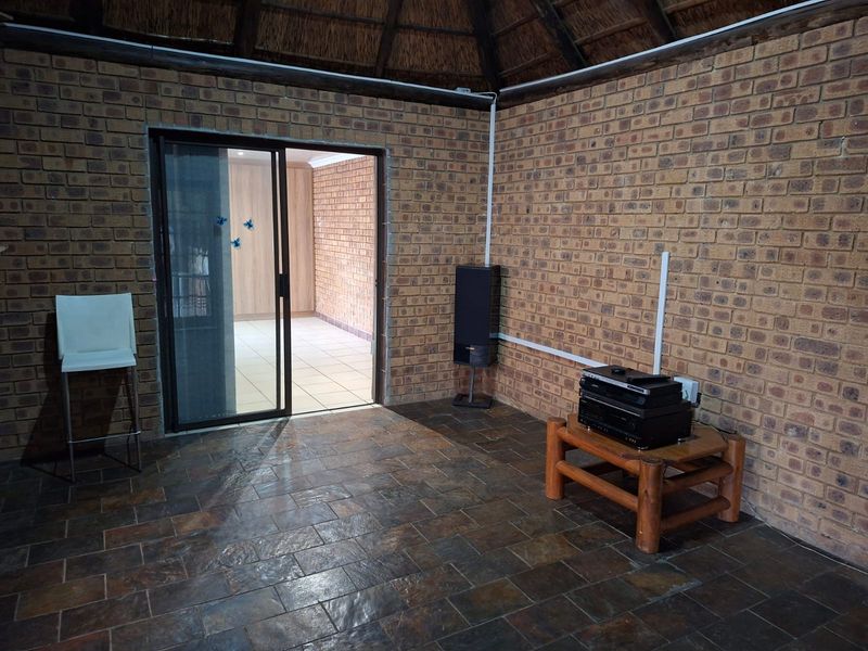 Living area featuring rustic exposed brick walls, slate tile flooring, and a traditional thatched roof ceiling with access to an adjoining room.