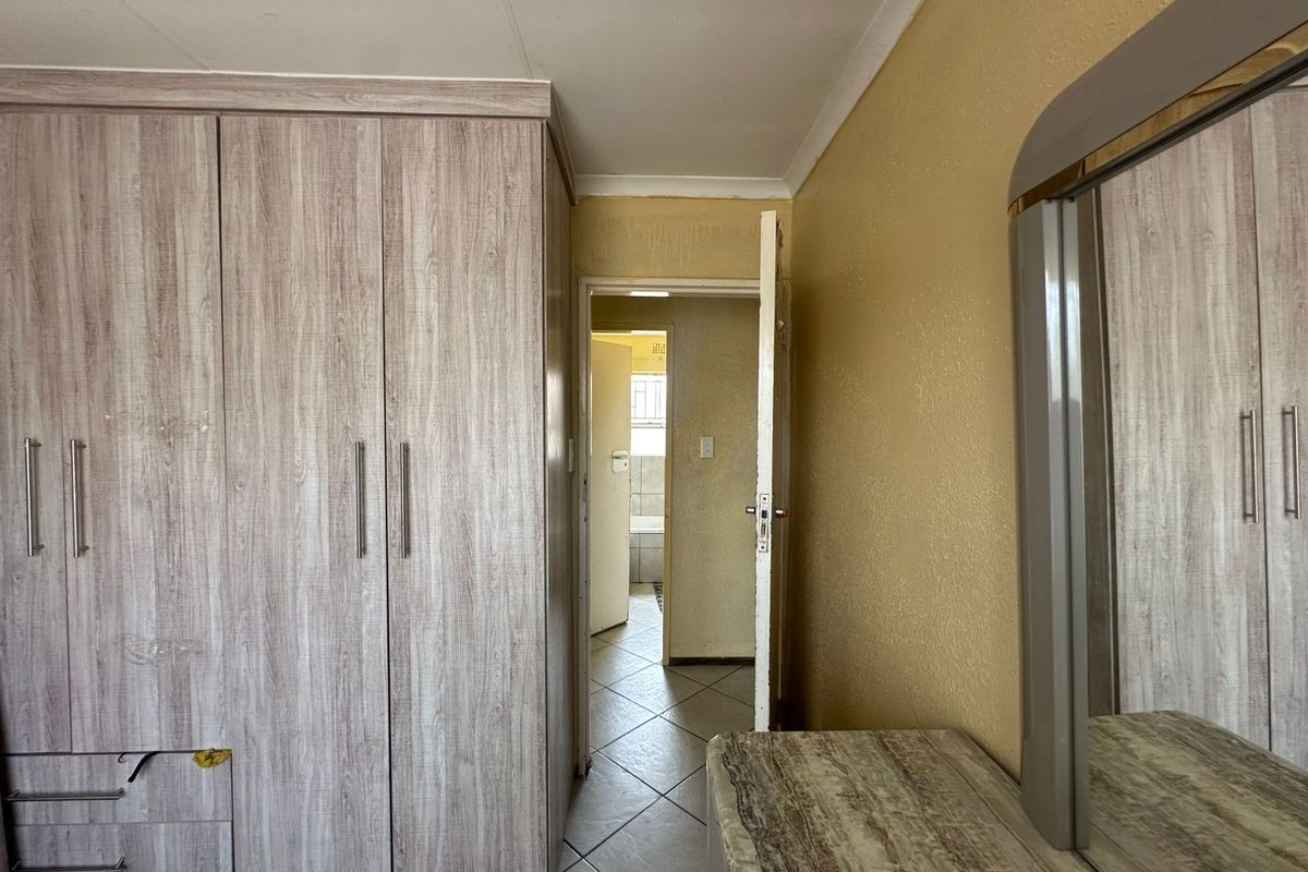 Bedroom featuring built-in wood-grain wardrobes and tiled flooring, with a doorway leading to an adjacent bathroom.