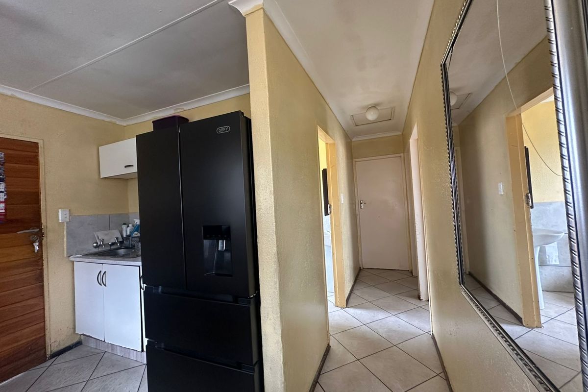 A view of a kitchen area and hallway featuring tiled flooring, built-in cabinetry, and access to adjacent rooms.