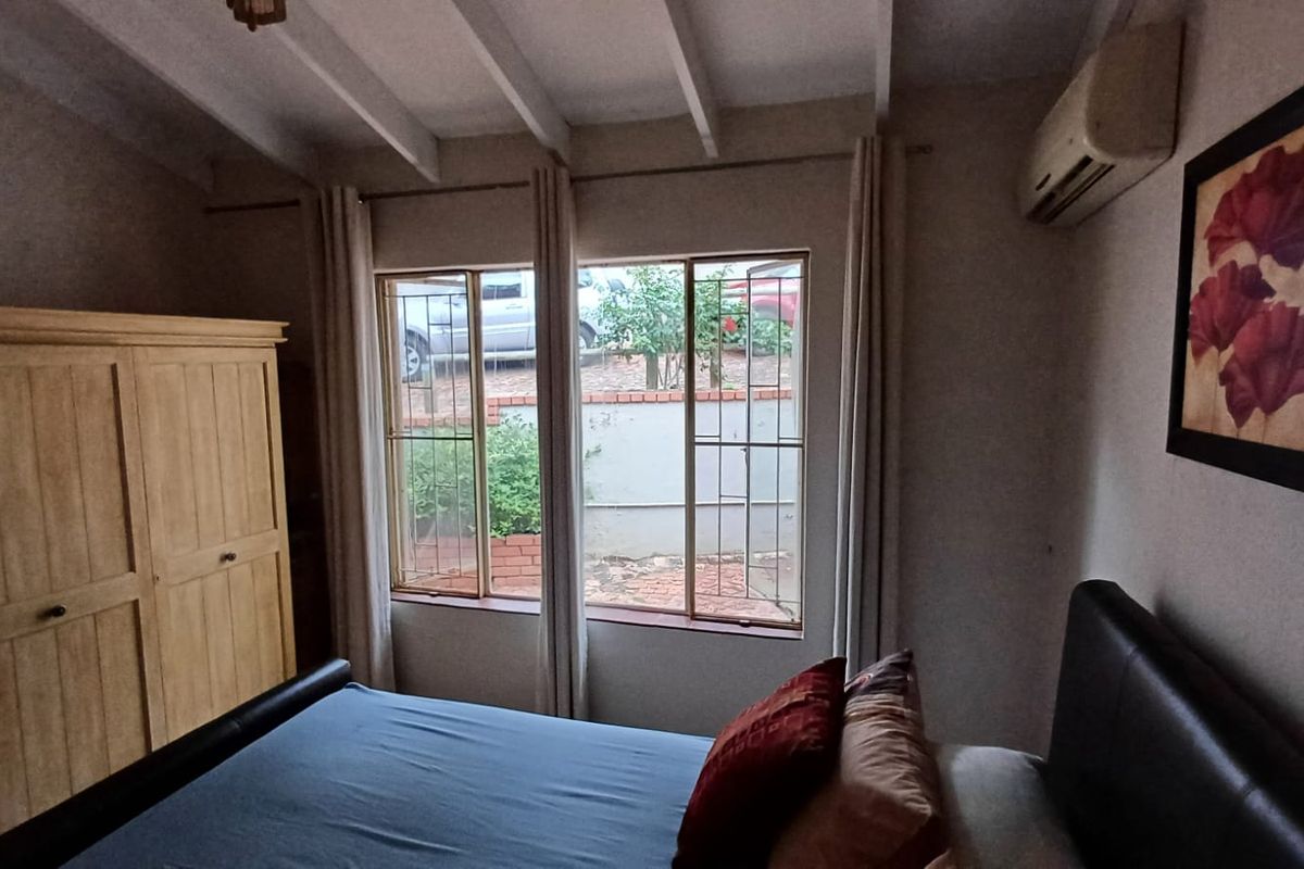 A bedroom featuring exposed ceiling beams, a wall-mounted air conditioning unit, and windows fitted with security bars.