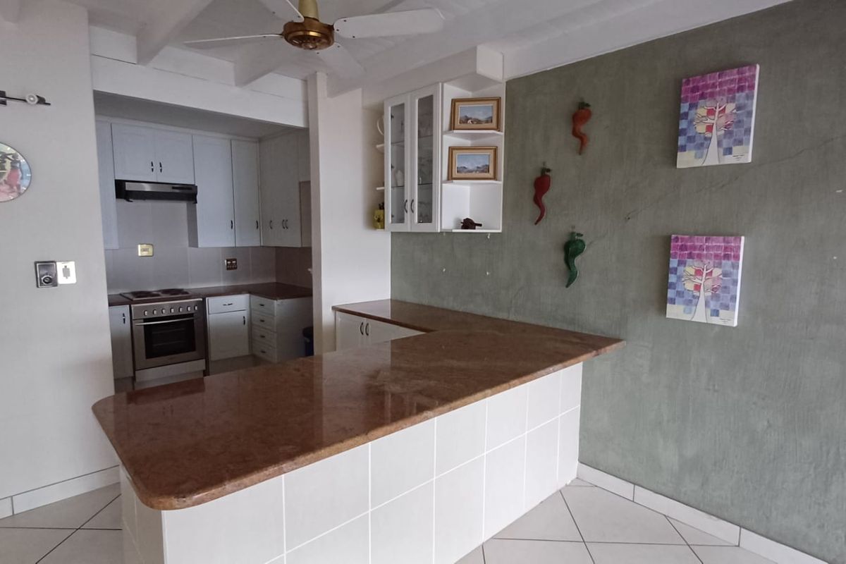 Kitchen featuring white cabinetry, stone countertops, a tiled breakfast bar, and integrated appliances, with a distinct feature wall.