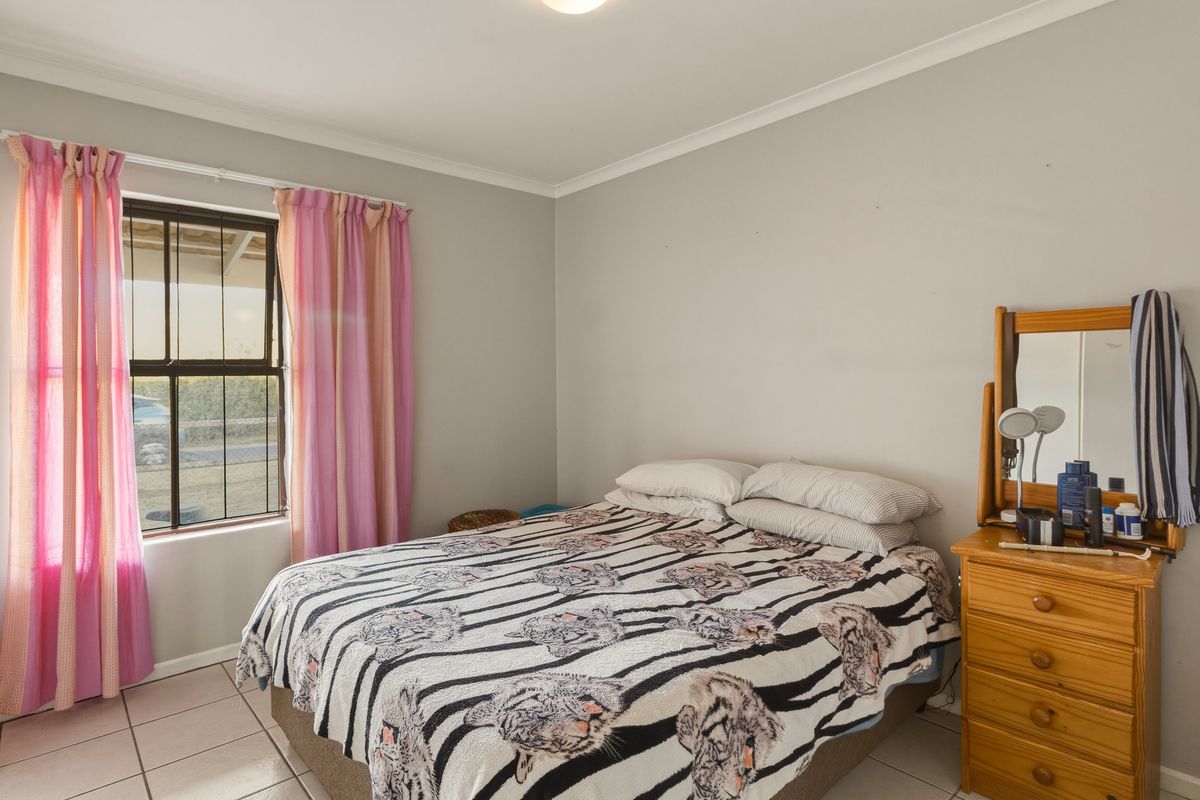 A standard bedroom featuring tiled flooring, neutral wall paint, and a window fitted with security bars.
