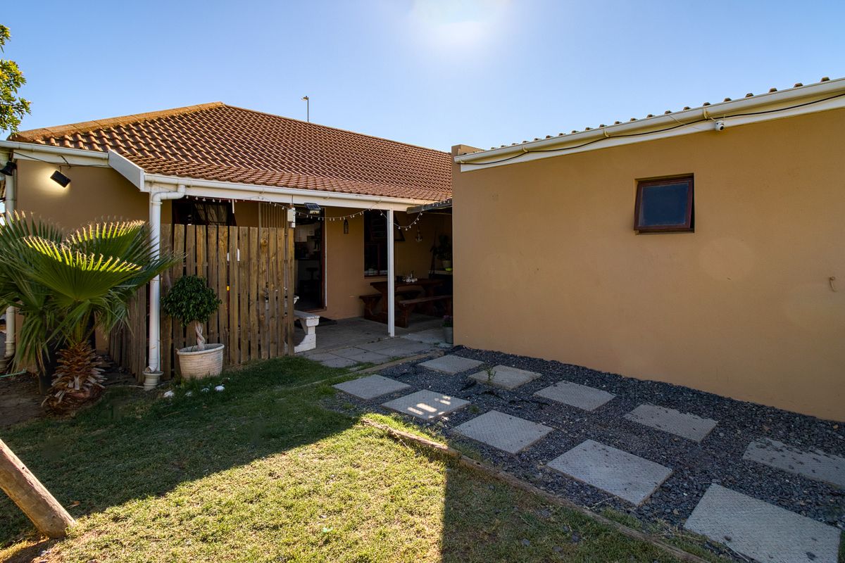 Rear view of the property featuring a covered patio area, paved garden path, and established lawn space.