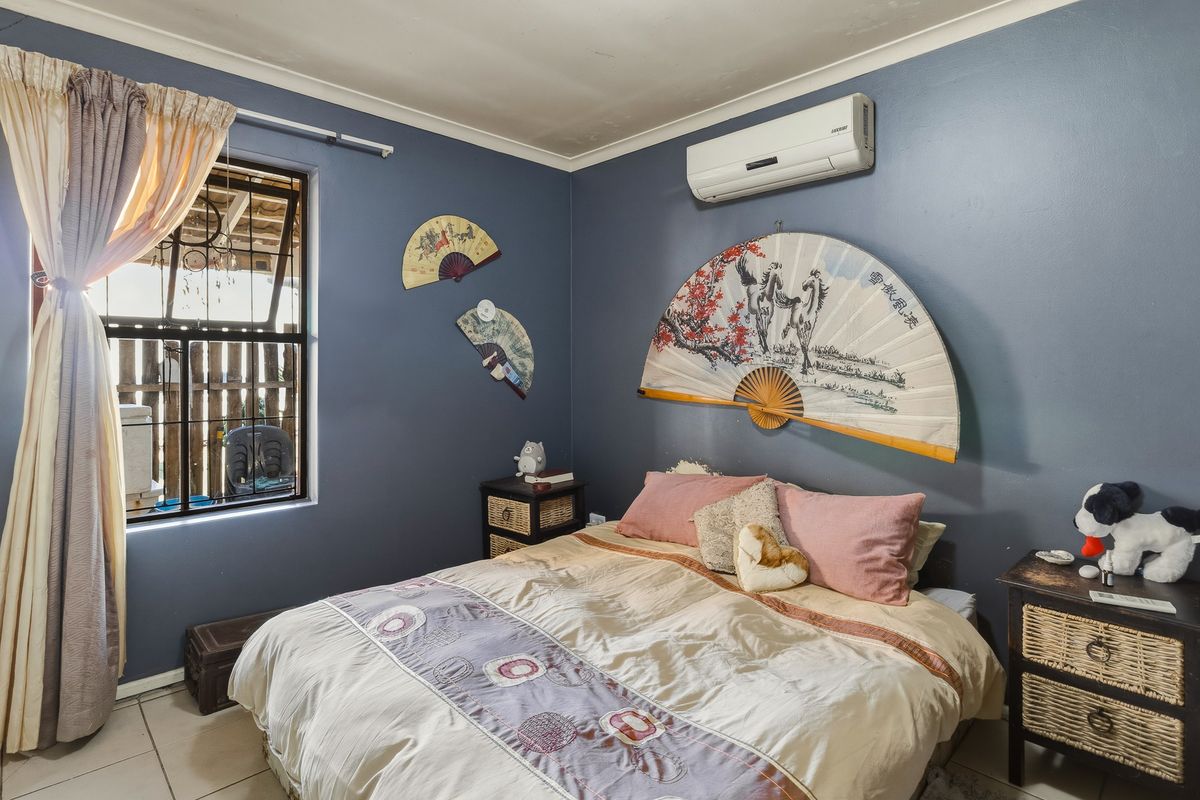 A bedroom featuring tiled flooring, a wall-mounted split-system air conditioner, and a window fitted with security bars.