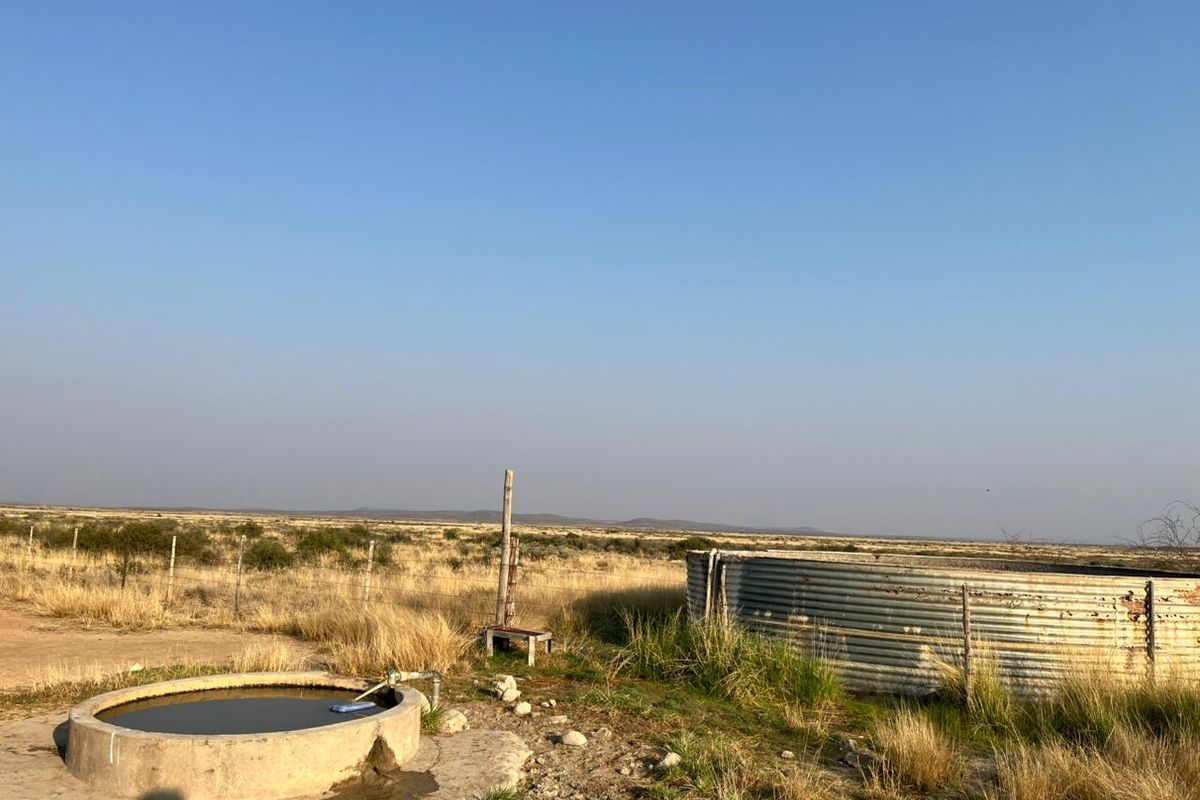 A rural farm landscape featuring a corrugated metal water storage tank and a concrete livestock water trough set in an open field.