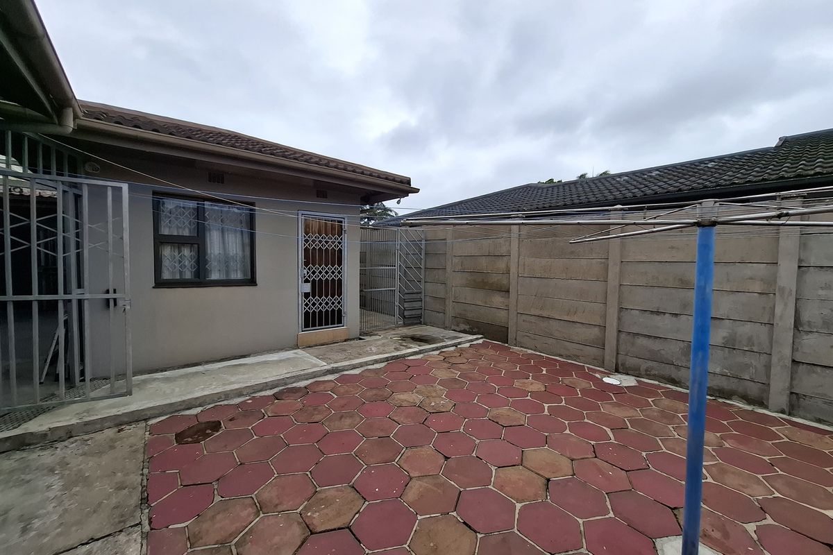A rear exterior view featuring a paved patio area, a precast concrete boundary wall, and secure access to the main dwelling.