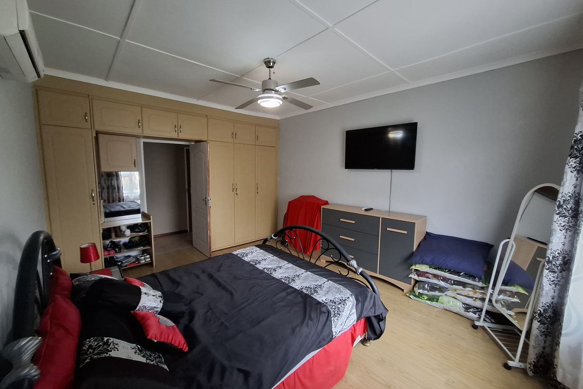 A bedroom featuring built-in cupboards, a ceiling fan, air conditioning, and laminate flooring.