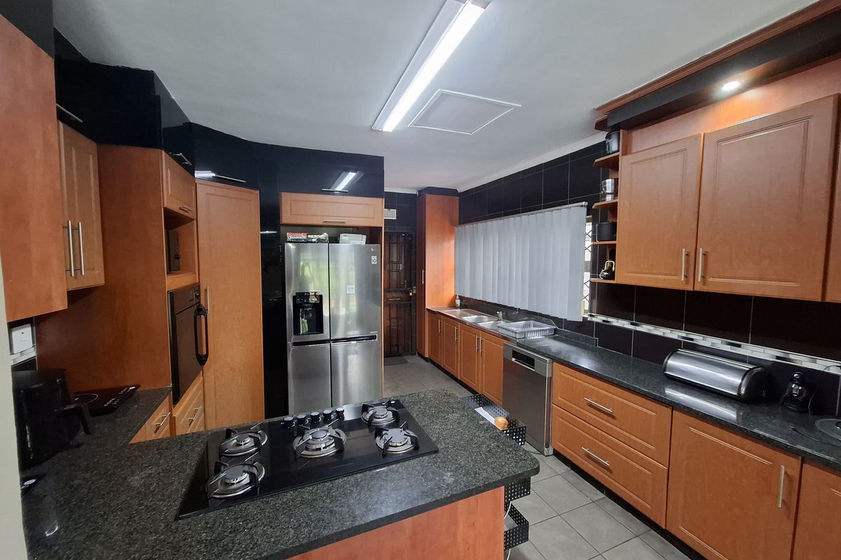A functional kitchen featuring wood-finish cabinetry, dark granite countertops, a central island with a gas hob, and tiled flooring.