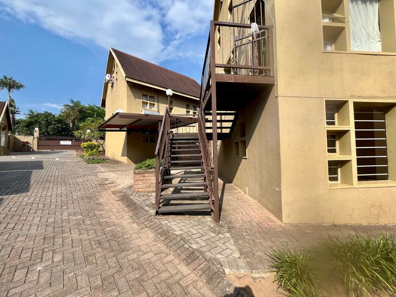 Exterior view of an apartment complex featuring a paved driveway, external staircase access, and traditional building architecture.