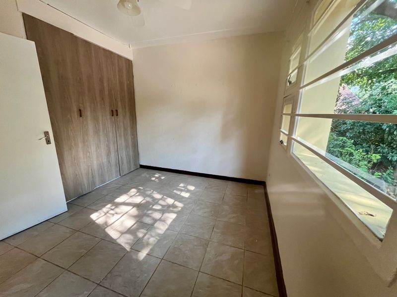 An empty bedroom featuring tiled flooring, built-in wooden cupboards, and large windows with security bars.
