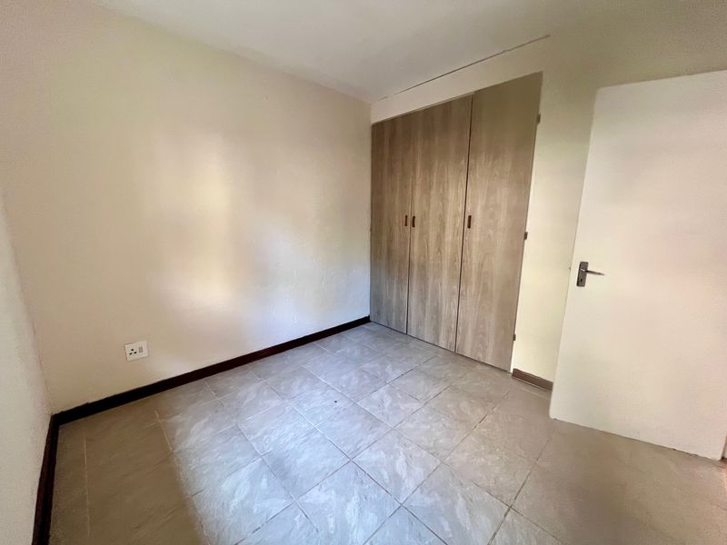 An empty bedroom featuring tiled flooring and built-in wooden cupboards, providing a neutral canvas for personalization.