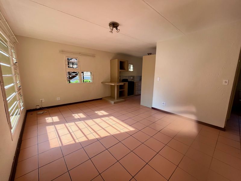 An open-plan living and kitchen area featuring tiled flooring, built-in cabinetry, and louvered windows, offering a blank canvas for renovation and interior design.