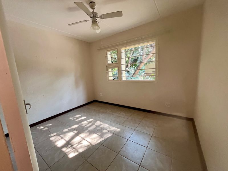 An empty bedroom featuring tiled flooring, a ceiling fan, and a window fitted with security bars.