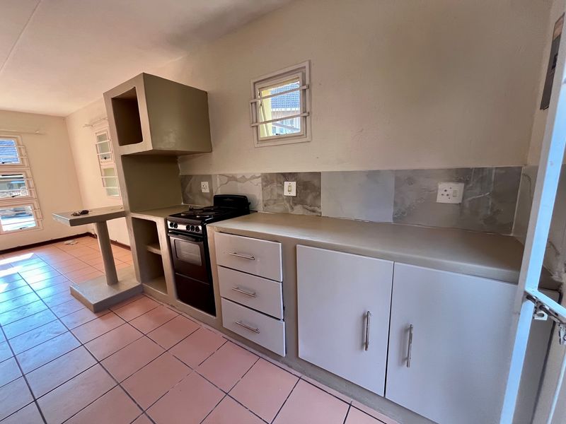 A functional kitchen featuring built-in cabinetry, a tiled backsplash, and a freestanding stove, with tiled flooring throughout the space.