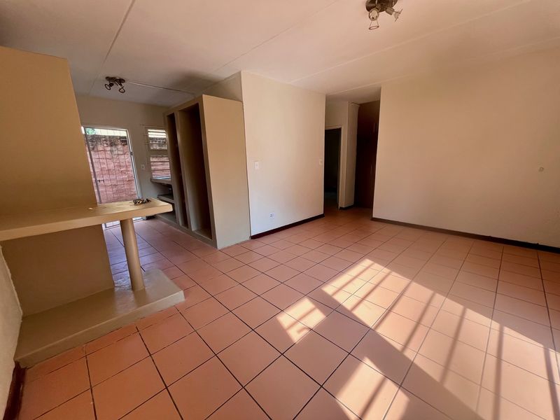 An empty open-plan living area featuring tiled flooring, a built-in breakfast counter, and integrated shelving units, offering a blank canvas for renovation.