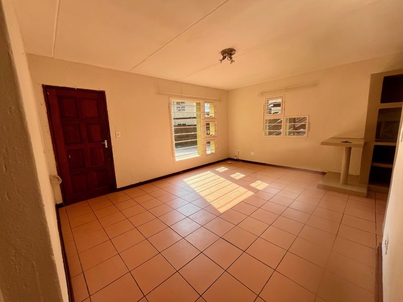 An empty living room featuring ceramic floor tiles, security bars on windows, and a built-in shelving unit, offering a blank canvas for renovation.