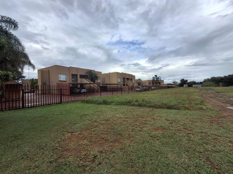 Exterior view of a townhouse complex featuring multiple units with carports, external staircases, and perimeter fencing set against a large open grass area.