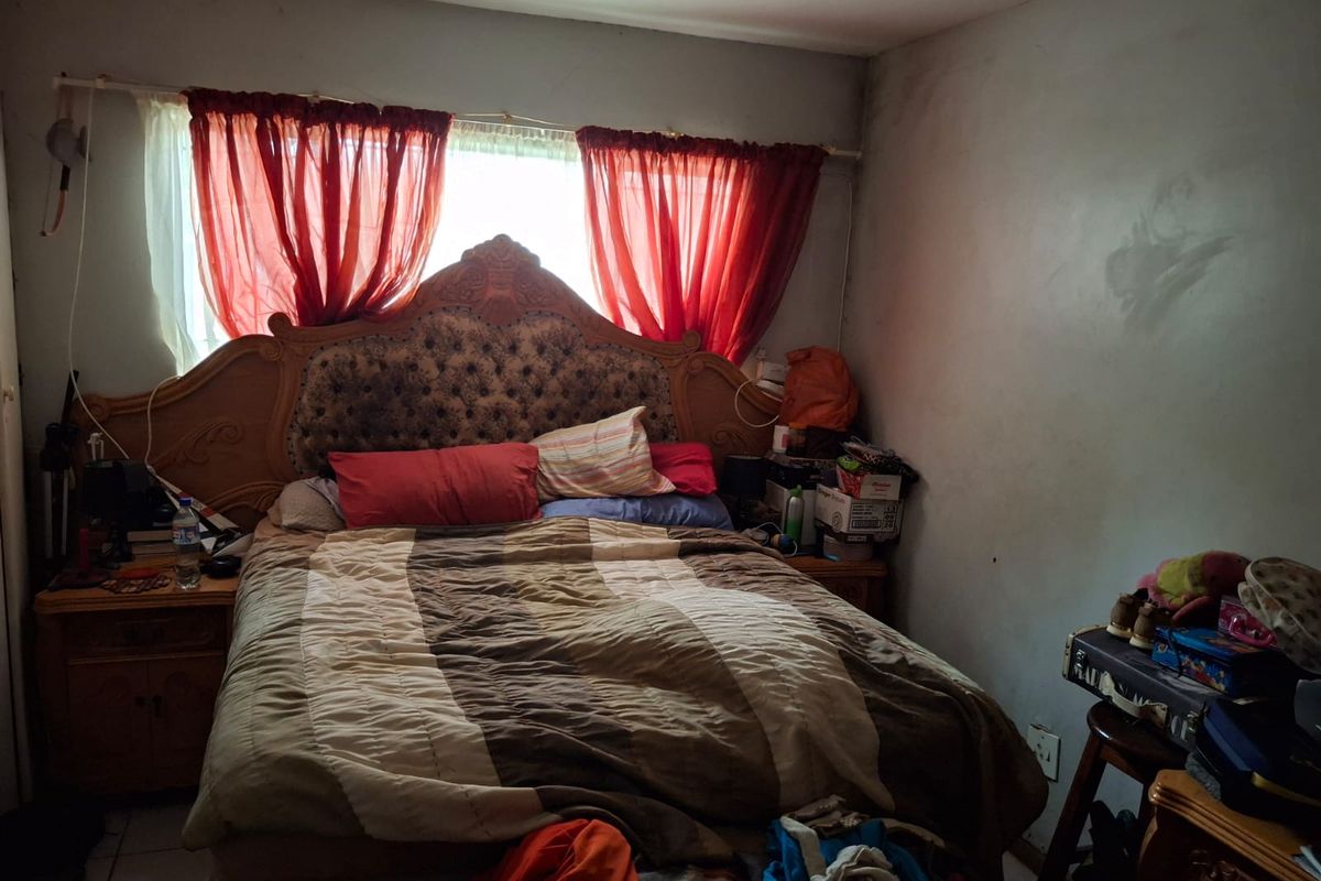 A bedroom featuring tiled flooring and a window, currently showing signs of wear including wall staining and peeling paint.