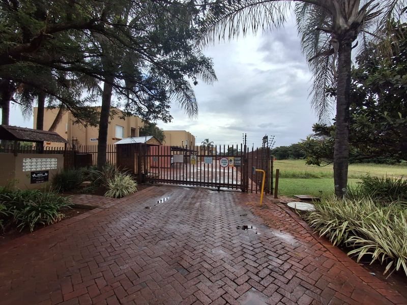Secure gated entrance to the townhouse complex featuring brick paving, metal security gates, and established garden landscaping.