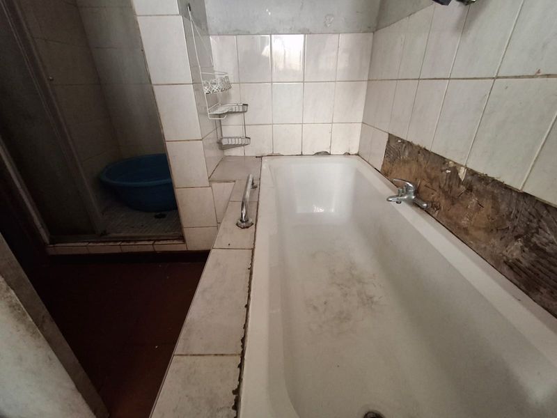A dated bathroom featuring a built-in bathtub and separate shower enclosure, currently requiring significant repairs to wall tiling and finishes.