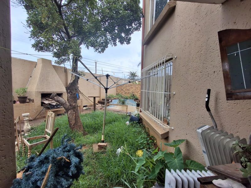 Rear garden area featuring a built-in braai, swimming pool, and security-barred windows, requiring landscaping and maintenance to improve the outdoor living space.