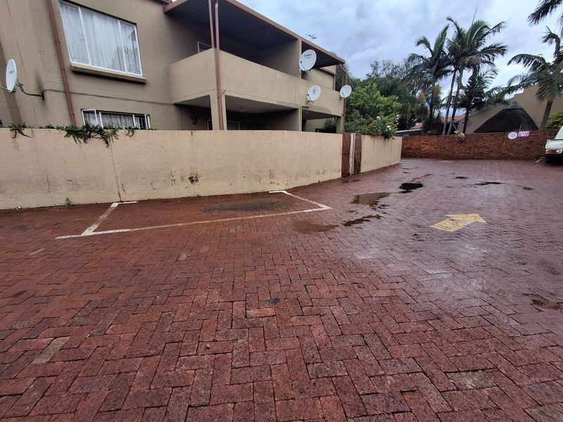 Exterior view of a townhouse complex featuring a paved driveway, parking bays, and a multi-story building with balconies.