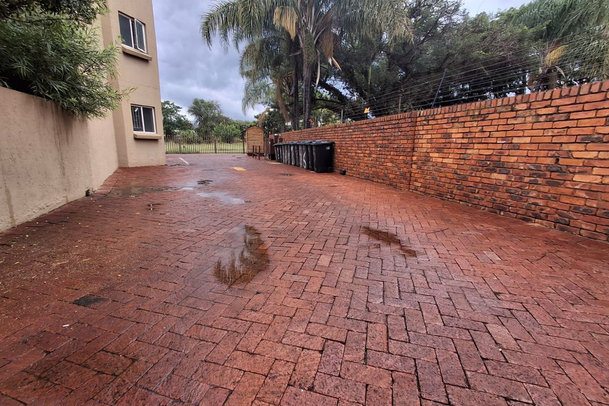 A paved rear courtyard area featuring a brick boundary wall with electric fencing and access to the side of the townhouse building.