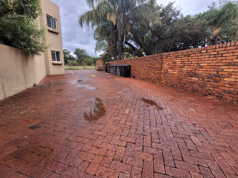 A paved rear courtyard area featuring a brick boundary wall with electric fencing and access to the side of the townhouse building.