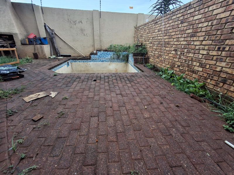 Outdoor pool area featuring brick paving and boundary walls, currently requiring maintenance and restoration of the swimming pool and surrounding landscaping.