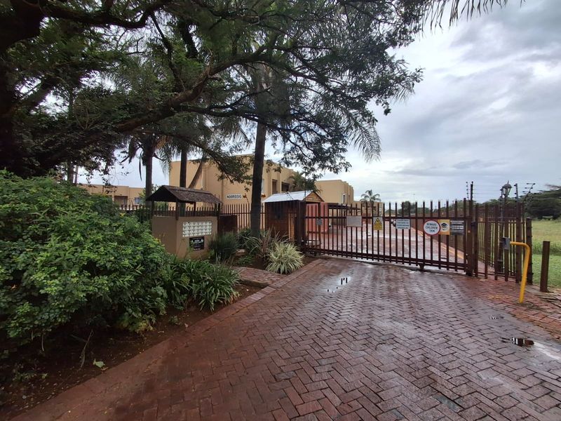 Front entrance view of the townhouse complex featuring a secure gated access point, brick paved driveway, and perimeter security fencing.